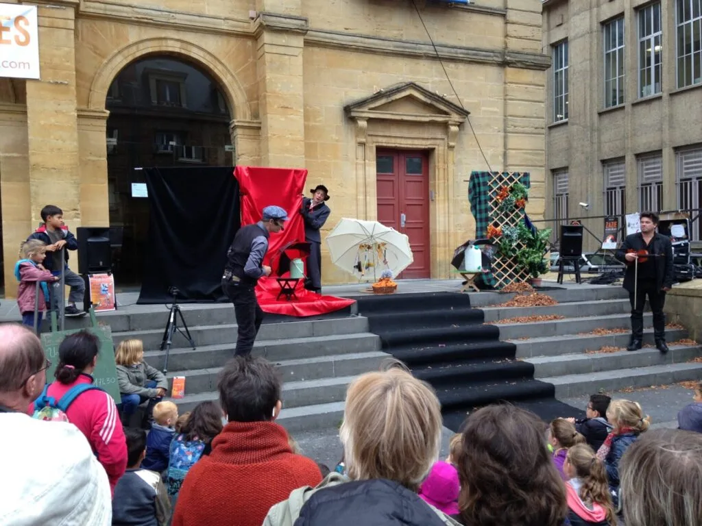 Décor posé en haut des marches du théâtre de Charleville-Mézières pendant le Festival des théâtres de Marionnettes. Le jeu se déroule dans les marches. Là le comédien monte, tandis que le violoniste attend. Une foule regarde le spectacle