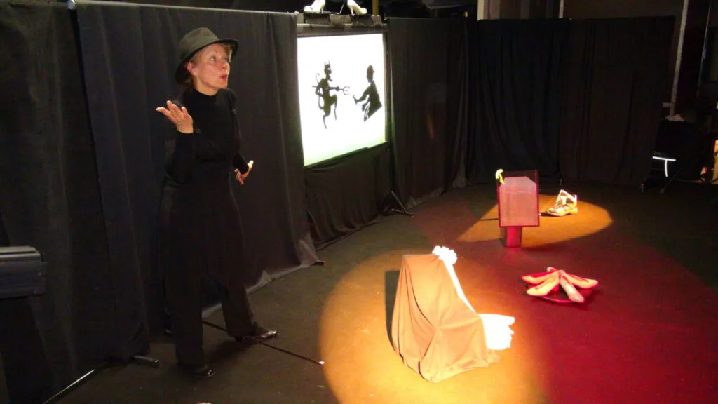 Image avec éclairage orangée dans la suite des tableaux avec Liliane Plouzeau, comédienne en répétition dans son atelier dans un décor identique pour les 4 tableaux, seuls des éclairages et les postures diffèrent.