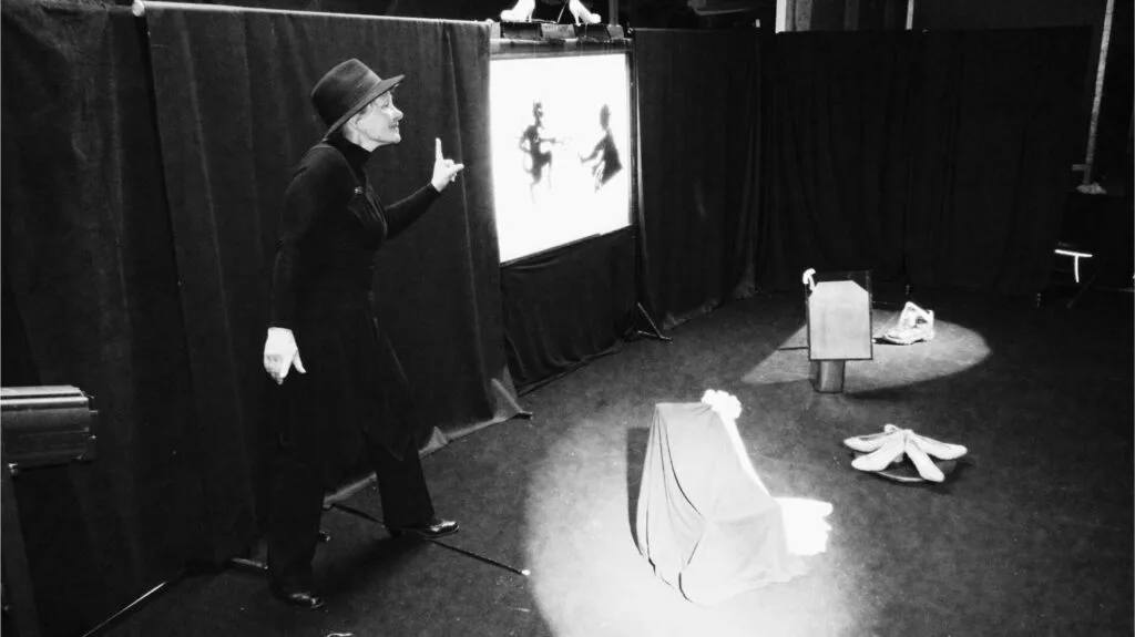 Image en noir et blanc une esthétique avec les 4 tableaux représentant la marionnettiste, comédienne. Ici, elle attire l’attention du public imaginaire en pointant du doigt l’écran sur lequel on peut voir le diable, le cordonnier en ombres