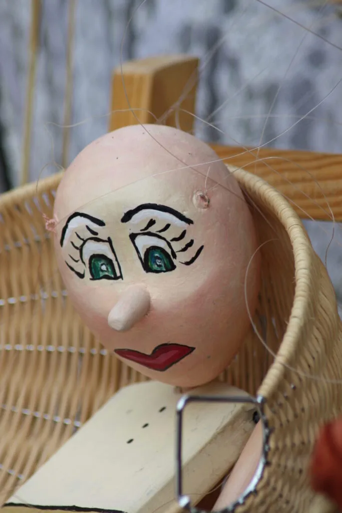 Buste de Tim la marionnette adossée dans une corbeille d'osier. Sa bouche rouge forme un coeur, son nez est pointu comme Pinocchio. Le plus frappant, ce sont ses yeux verts très expressifs. Au repos, Il a l'air très attentionné.