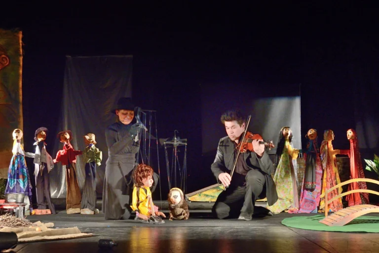 À genoux, la marionnettiste et le violoniste qui joue, encadrent deux marionnettes, l'une, Valentine vêtue de jaune et un hérisson. C'est le final. Autour d’eux, des marionnettes sur pied observent la scène finale sous une lumière douce