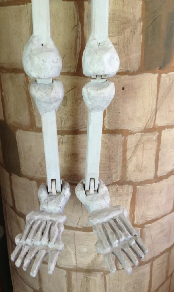 Deux jambes avec les pieds d'une marionnette- squelette fabriquées par Liliane Plouzeau, pendent sur un mur