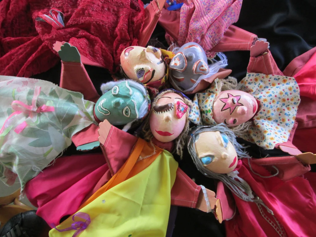 Marionnettes à gaines aux visages originaux avec des costumes et allongées en rond, têtes au centre, fabriquées dans le cadre d'un atelier avec un lycée et Liliane Plouzeau. Beaucoup de couleurs. Visuel attrayant.
