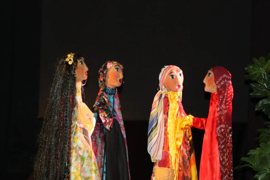 4 marionnettes sur pied, cadrées assez serrées aux costumes traditionnels tziganes, semblent commérer. Sur fond de scène noir, dans une chaude lumière, elles sont bien mises en valeur. Elles sont très belles.