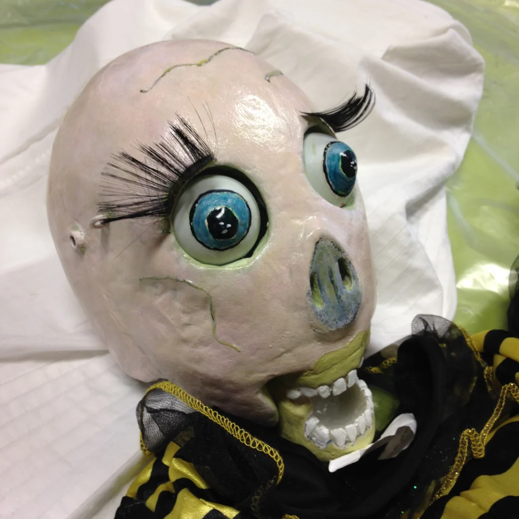 Gros plan sur le visage de la Mort Jaune avec ses gros yeux aux longs cils et son grand sourire avec son dentier blanc, son nez aplati. Que de joie !